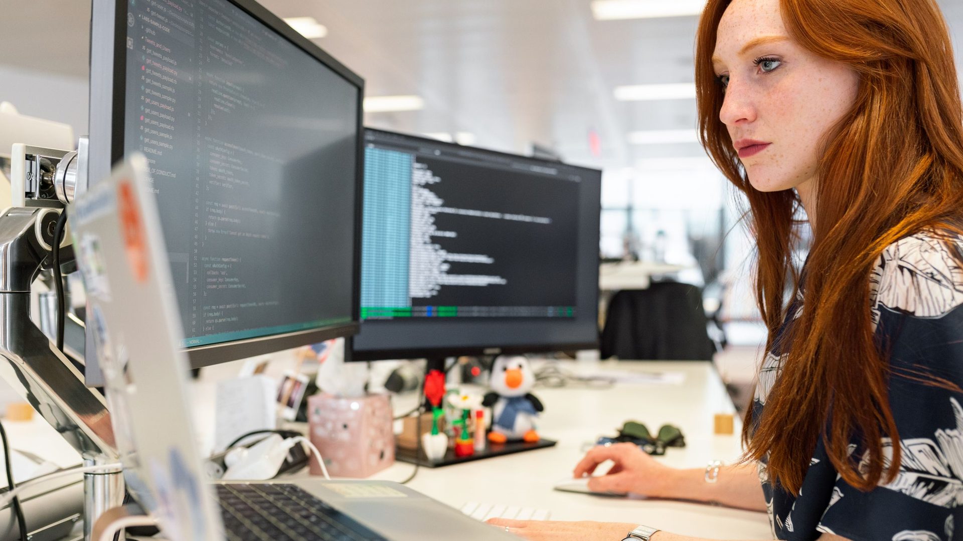 Mulher concentrada a programar em dois monitores num escritório moderno
